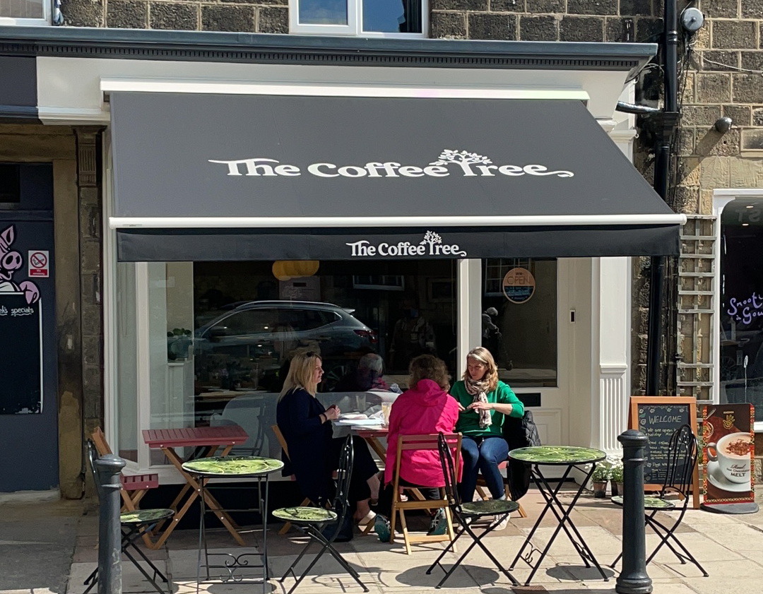 Customers dining outside The Coffee Tree café on Main Street in sunshine