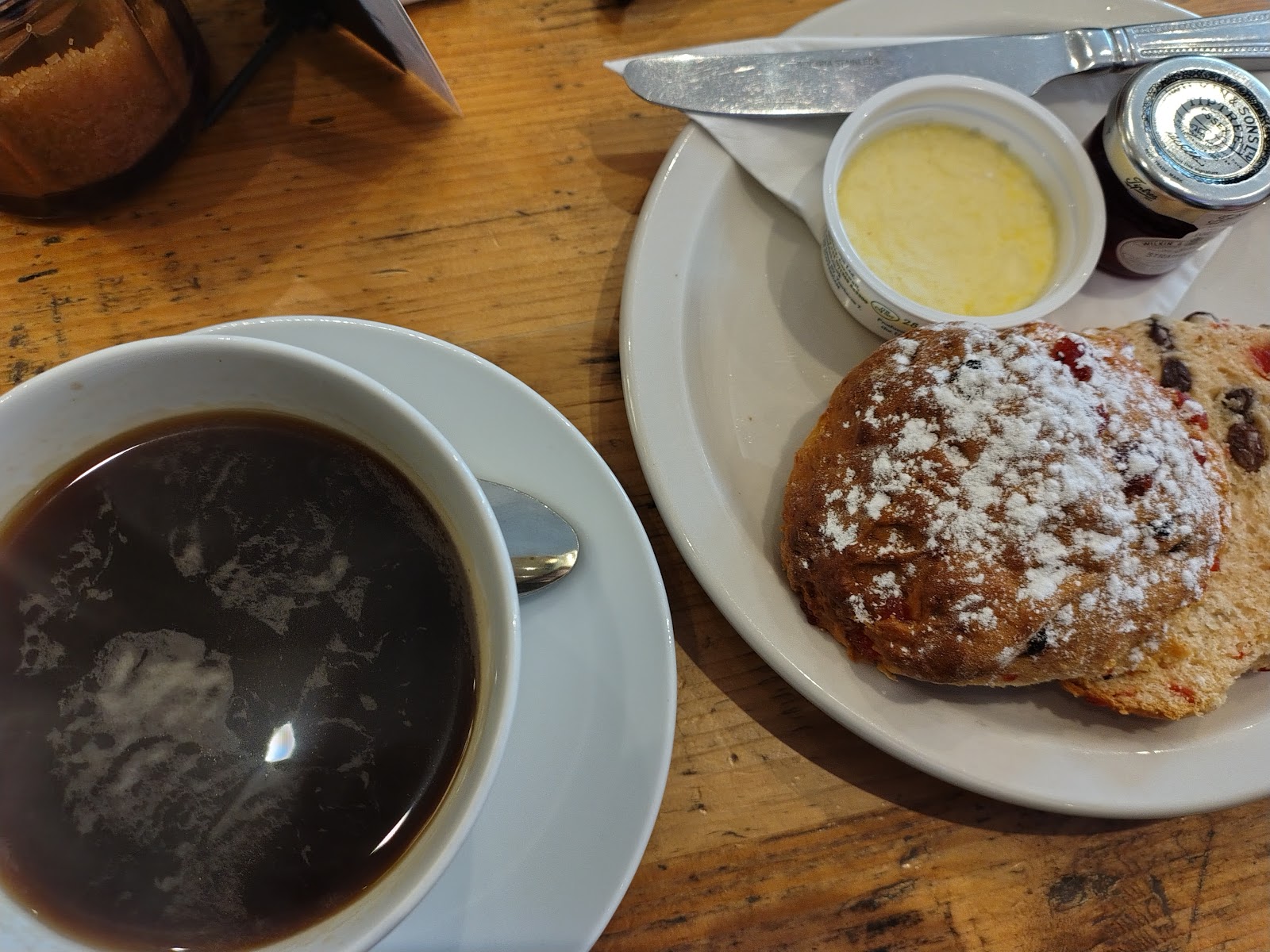 Fruit scone with clotted cream and jam alongside a black coffee